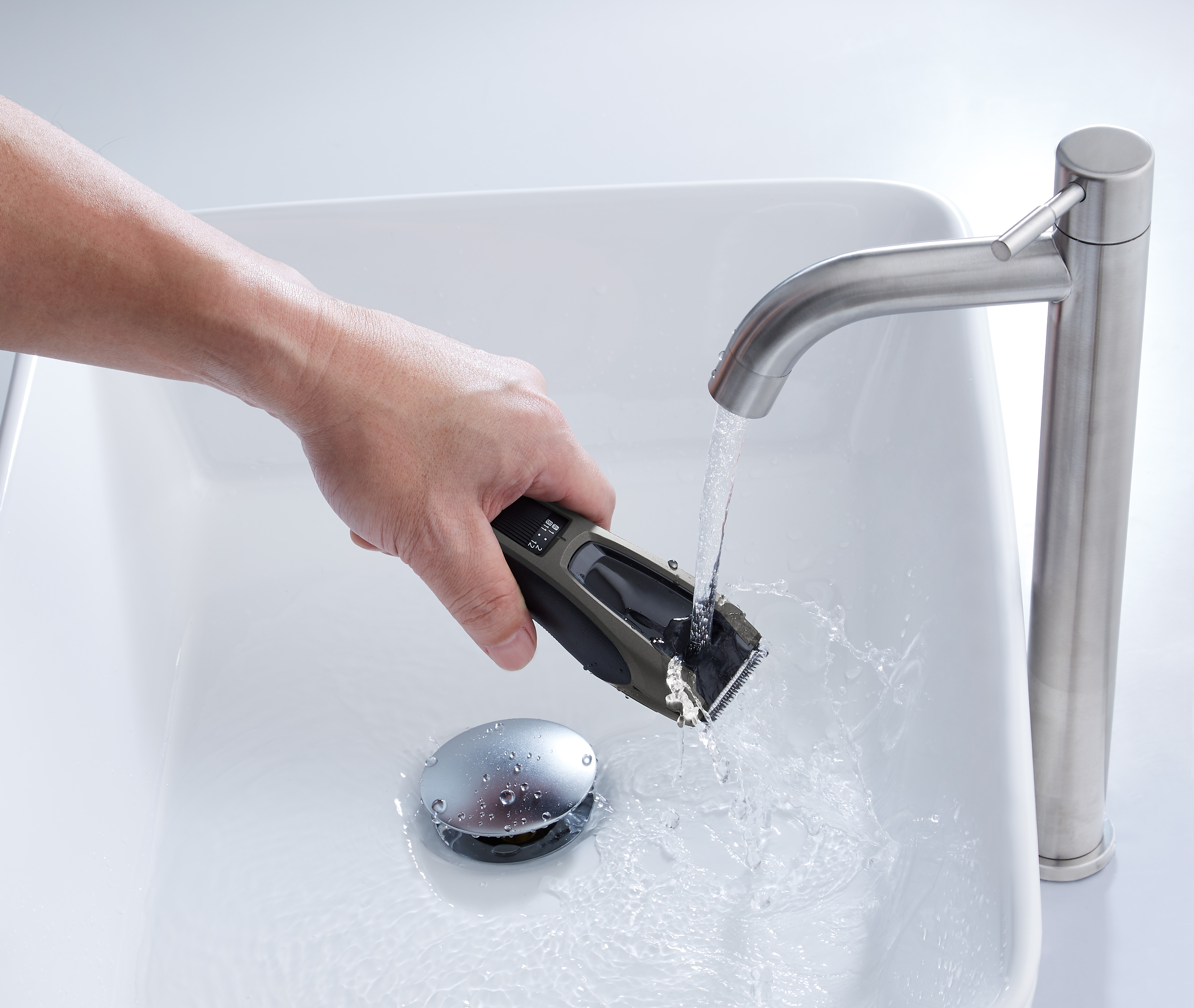 Ein Mann reinigt einen Rasierer unter fließendem Wasser im Waschbecken.