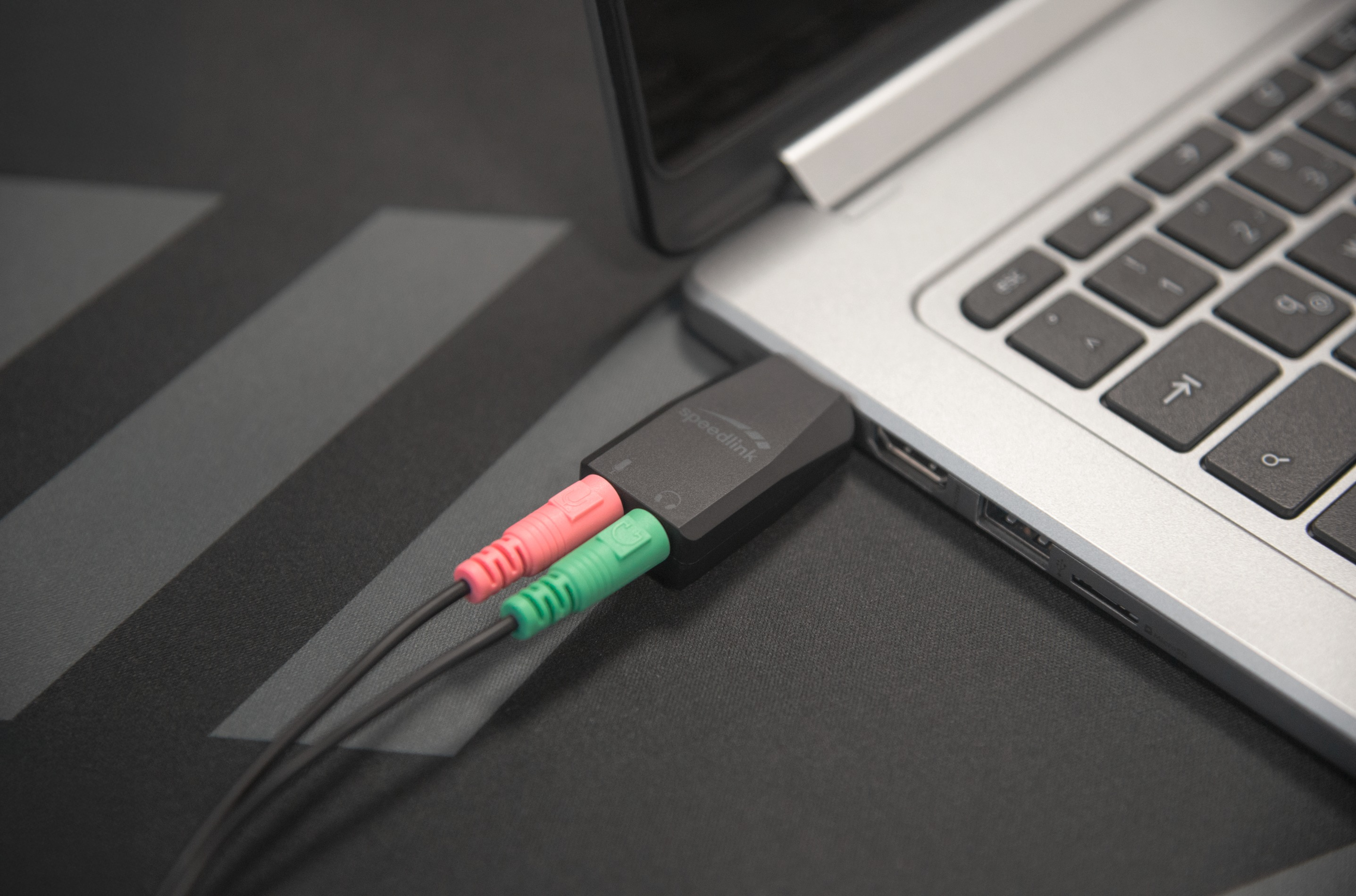 Ein schwarzer Adapter mit zwei Kabeln, rot und grün, steckt in einem Laptop.