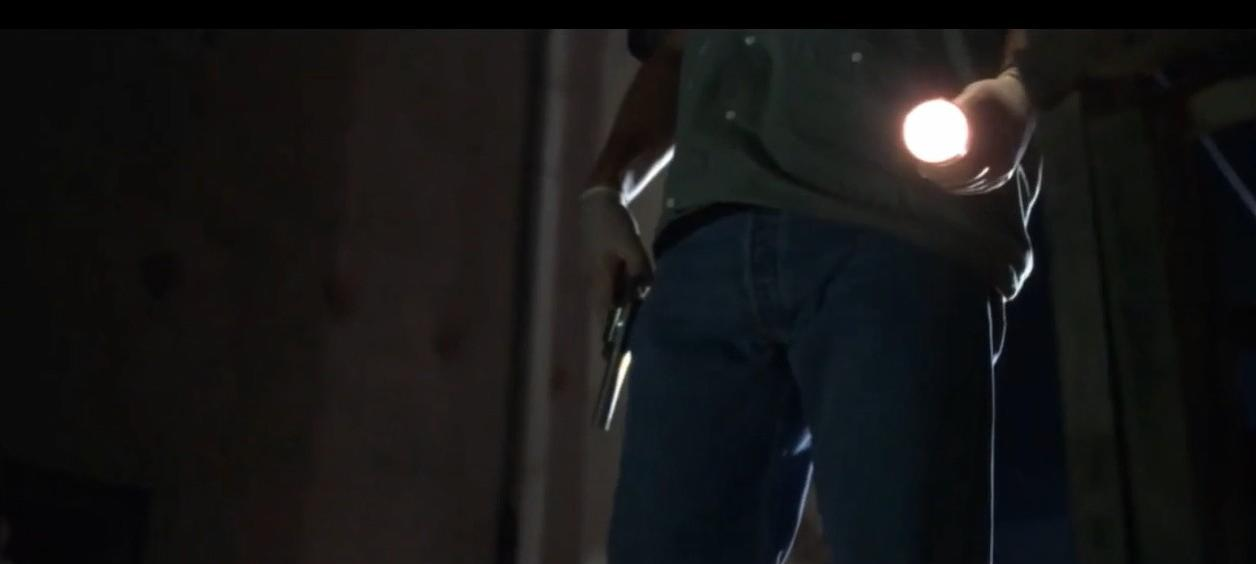 Person mit Taschenlampe und Waffe in dunkler Umgebung.