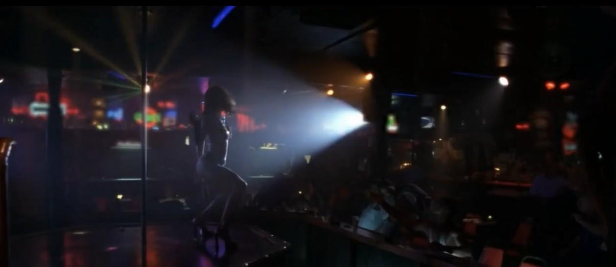Eine Frau tanzt auf einer Bühne in einem dunklen Nachtclub mit Lichtern.
