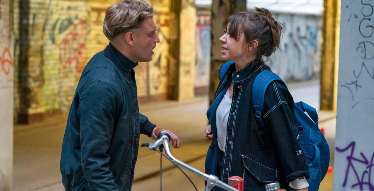 Ein Mann und eine Frau sprechen sich in einem graffitibesprühten Tunnel mit einem Fahrrad dazwischen.