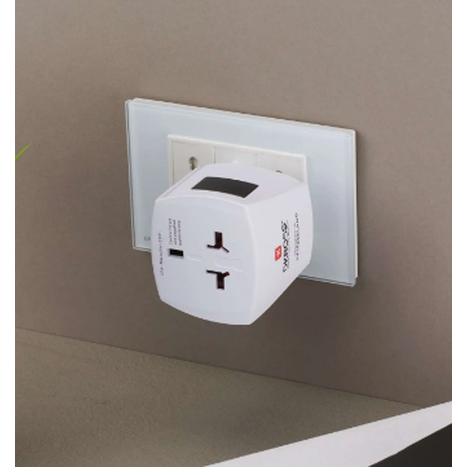 A white universal adapter plugged into a wall socket with a glass frame.