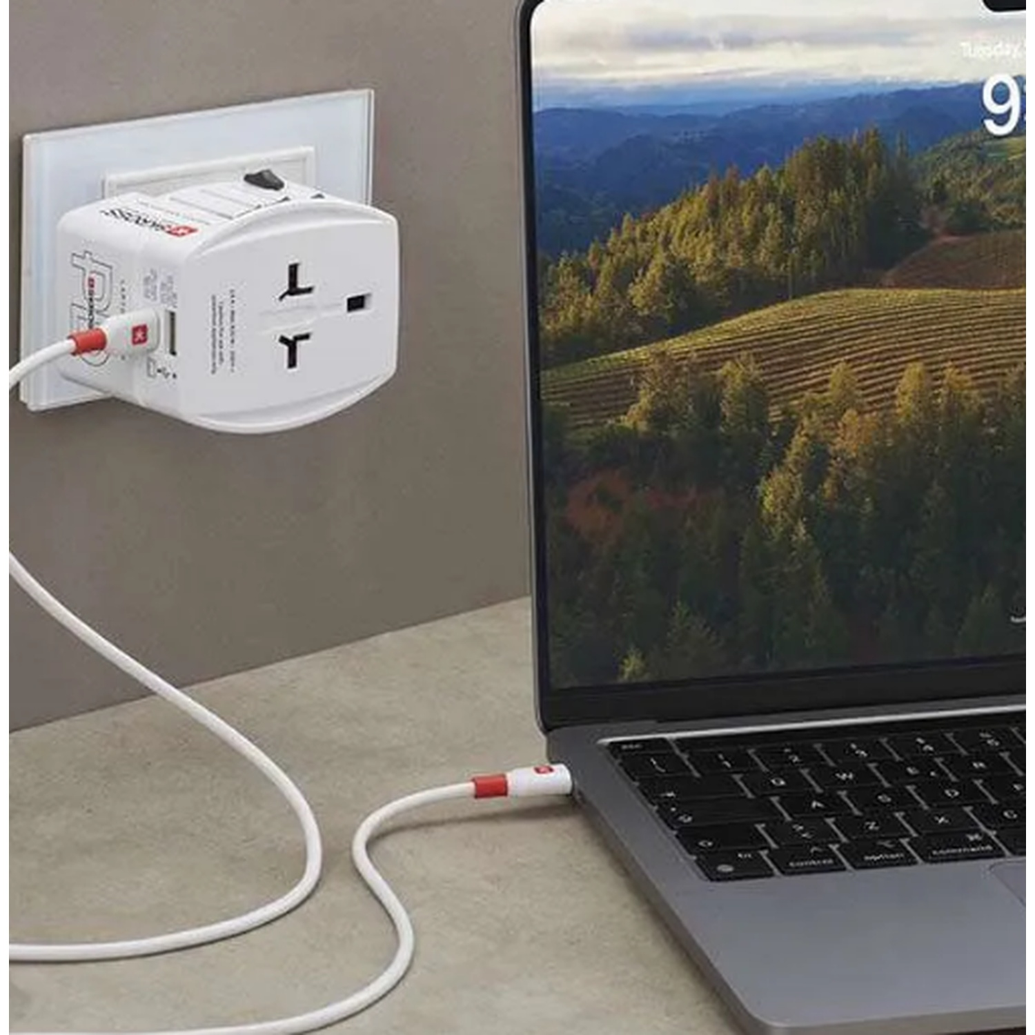 Un adaptateur de voyage blanc est branché à une prise murale, chargeant un ordinateur portable.