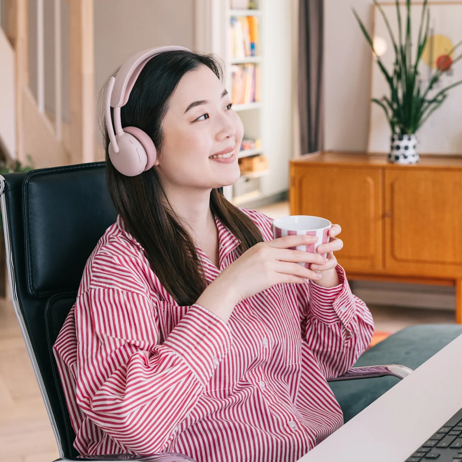 Une femme avec des écouteurs tient une tasse et sourit.