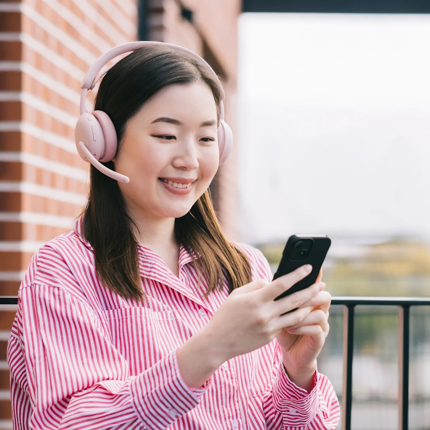 Une femme portant un casque et une chemise rayée regarde son téléphone.