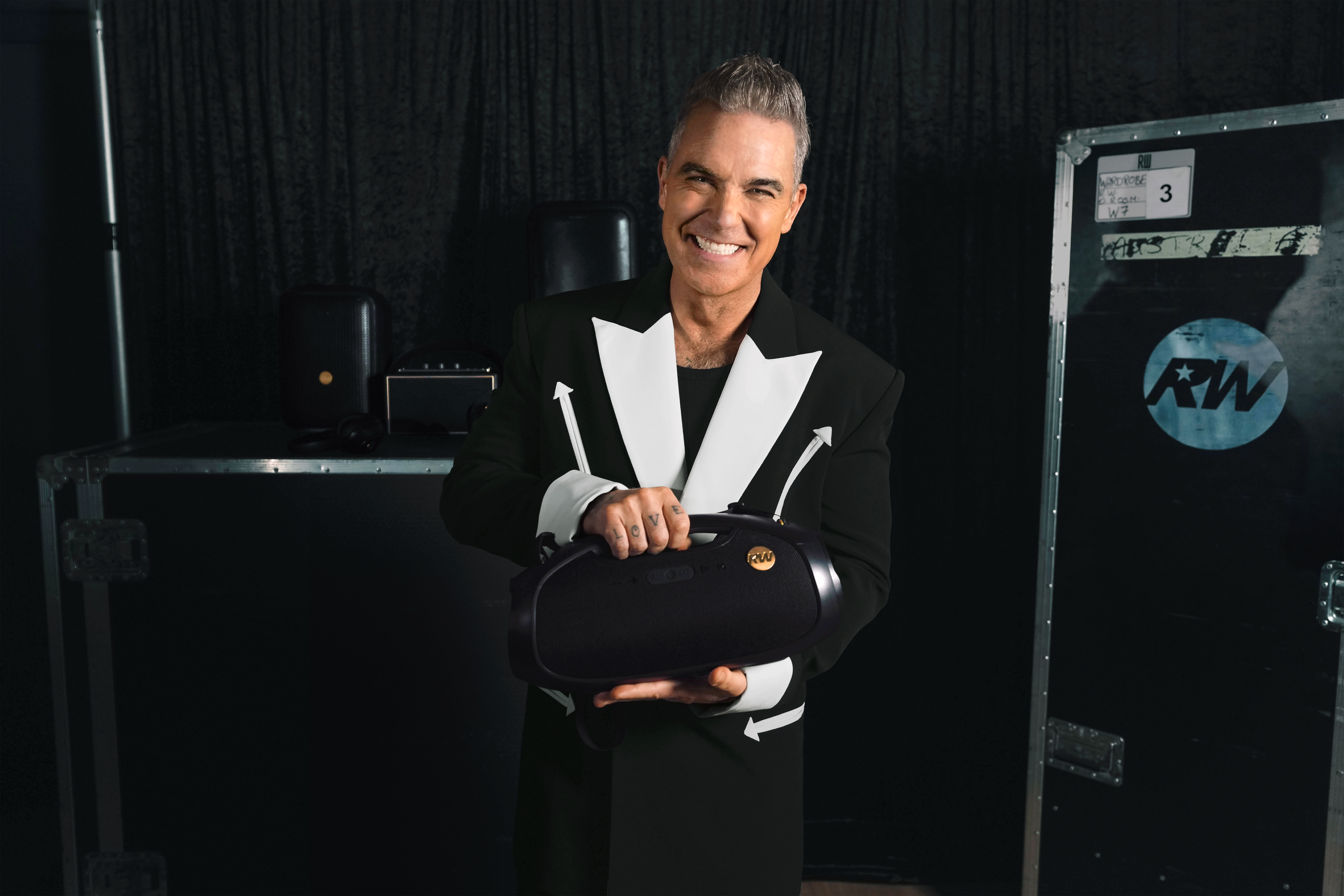 Homme en costume noir avec accents blancs tient une boombox noire.