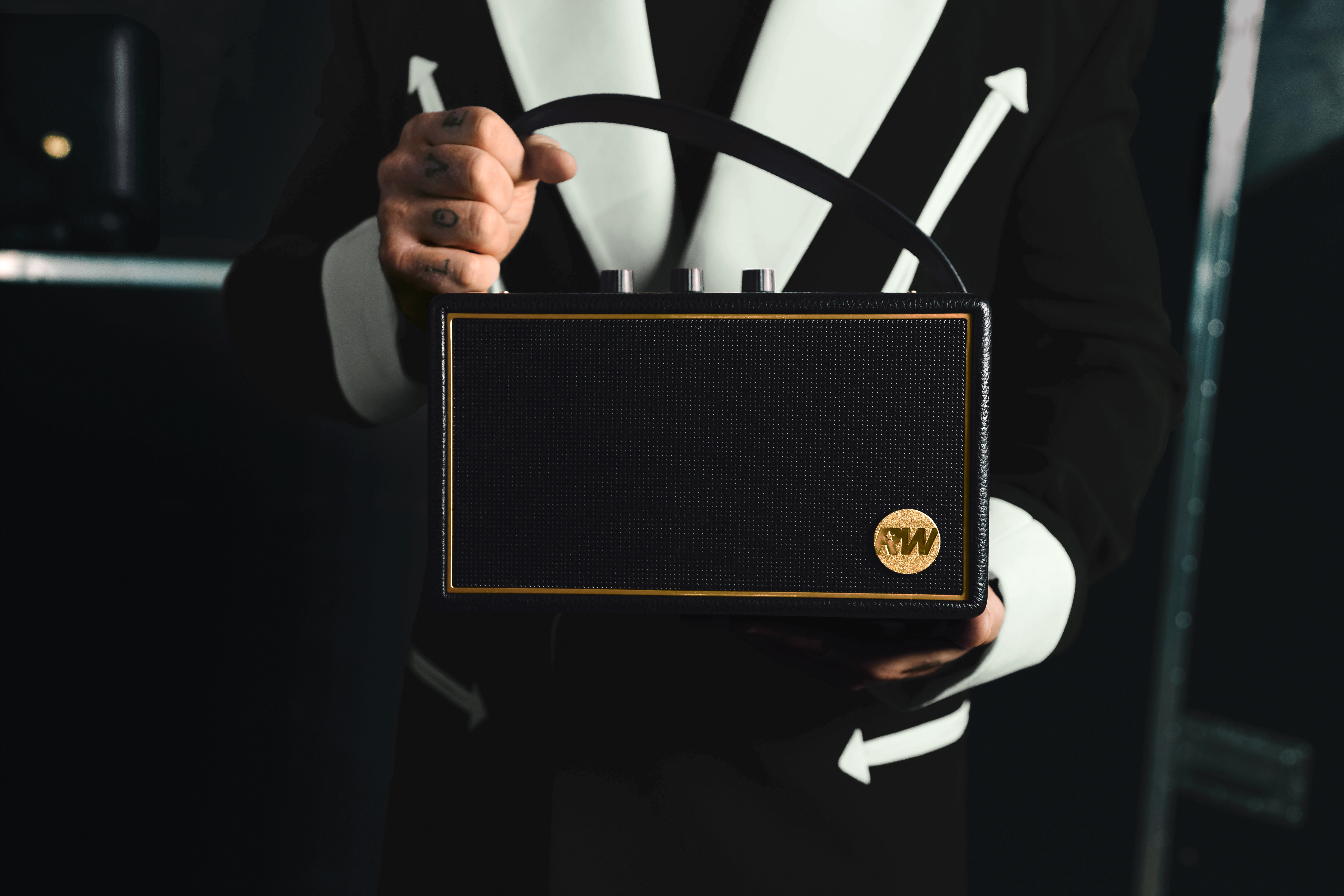 Une personne en costume noir et blanc tient un petit amplificateur noir à bordure dorée.