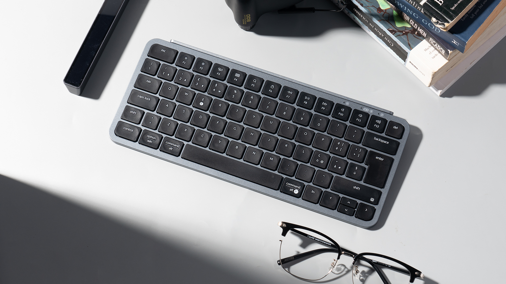 Graue Tastatur mit Büchern und Brille auf weißem Hintergrund.