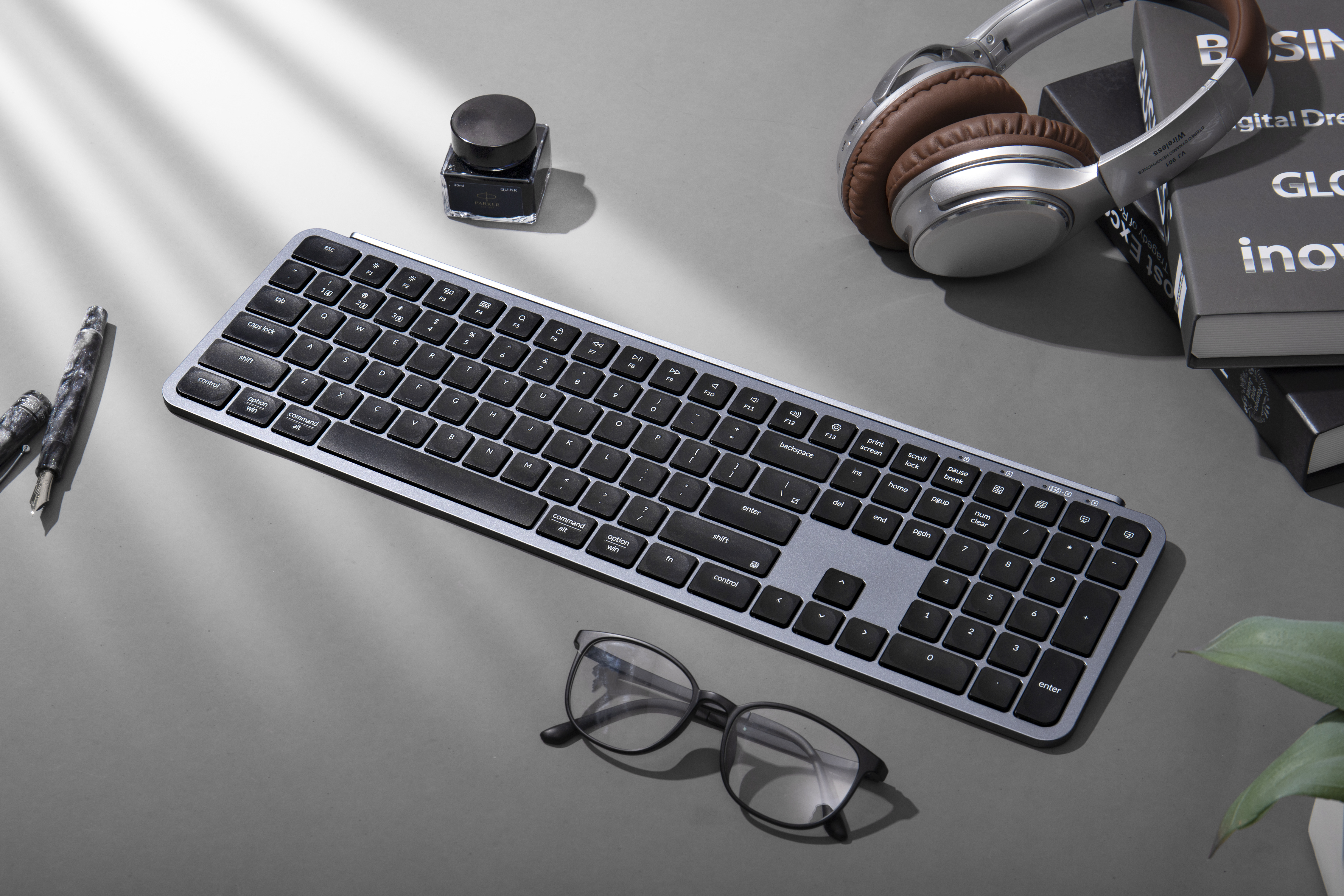 Schreibtischszene mit Tastatur, Stift, Tintenflasche, Kopfhörern und Büchern.