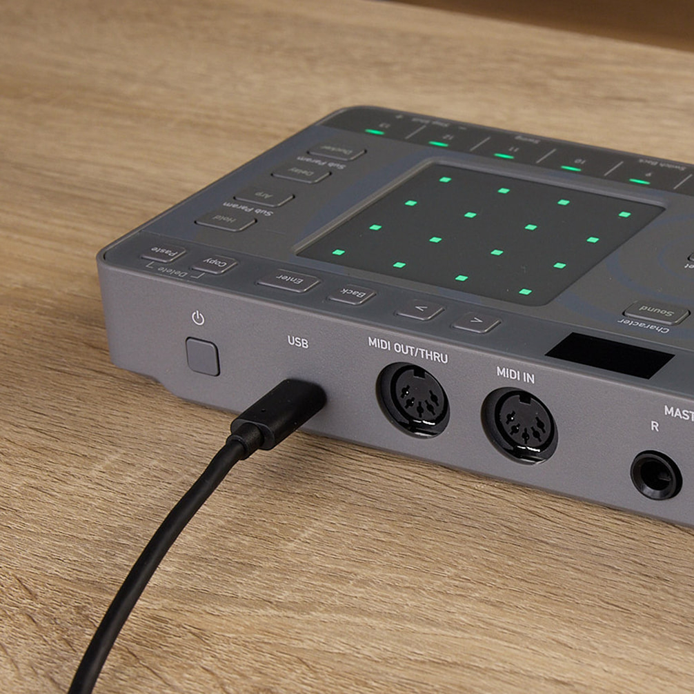 Szürke MIDI eszköz USB-kábellel és MIDI portokkal faasztalon.