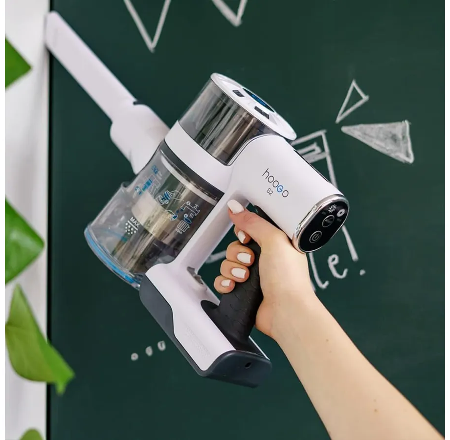 Eine Hand hält einen weißen Handstaubsauger vor einer grünen Tafel mit Kreidezeichnungen.