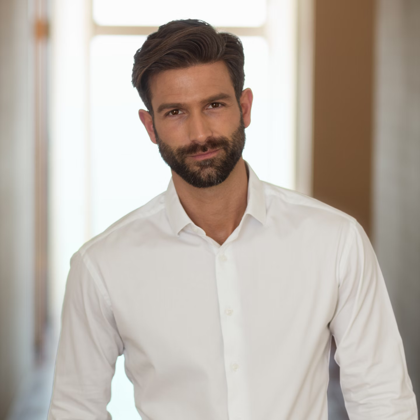 Un homme barbu en chemise blanche regarde la caméra.