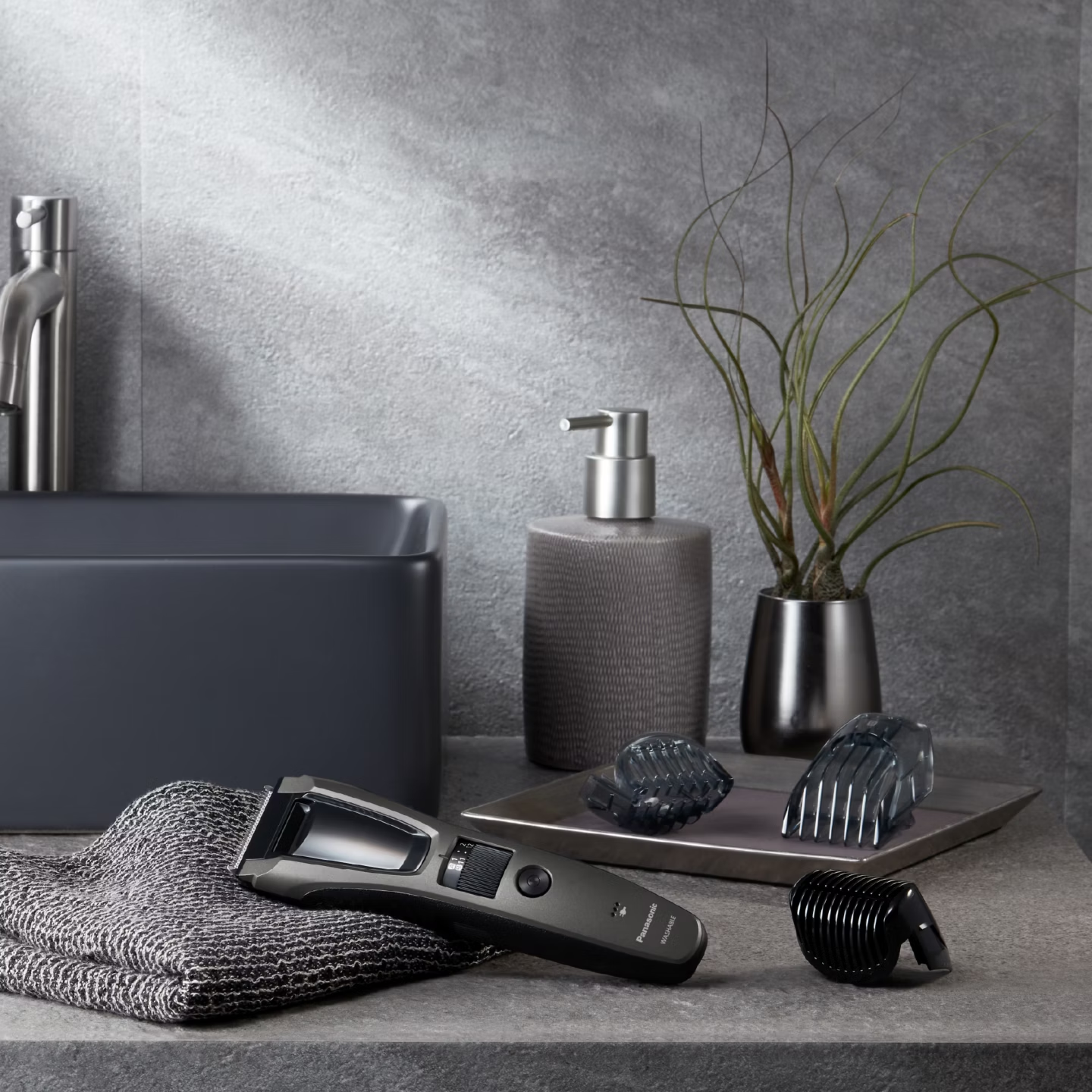 Une tondeuse à cheveux foncée avec accessoires sur une étagère de salle de bain.