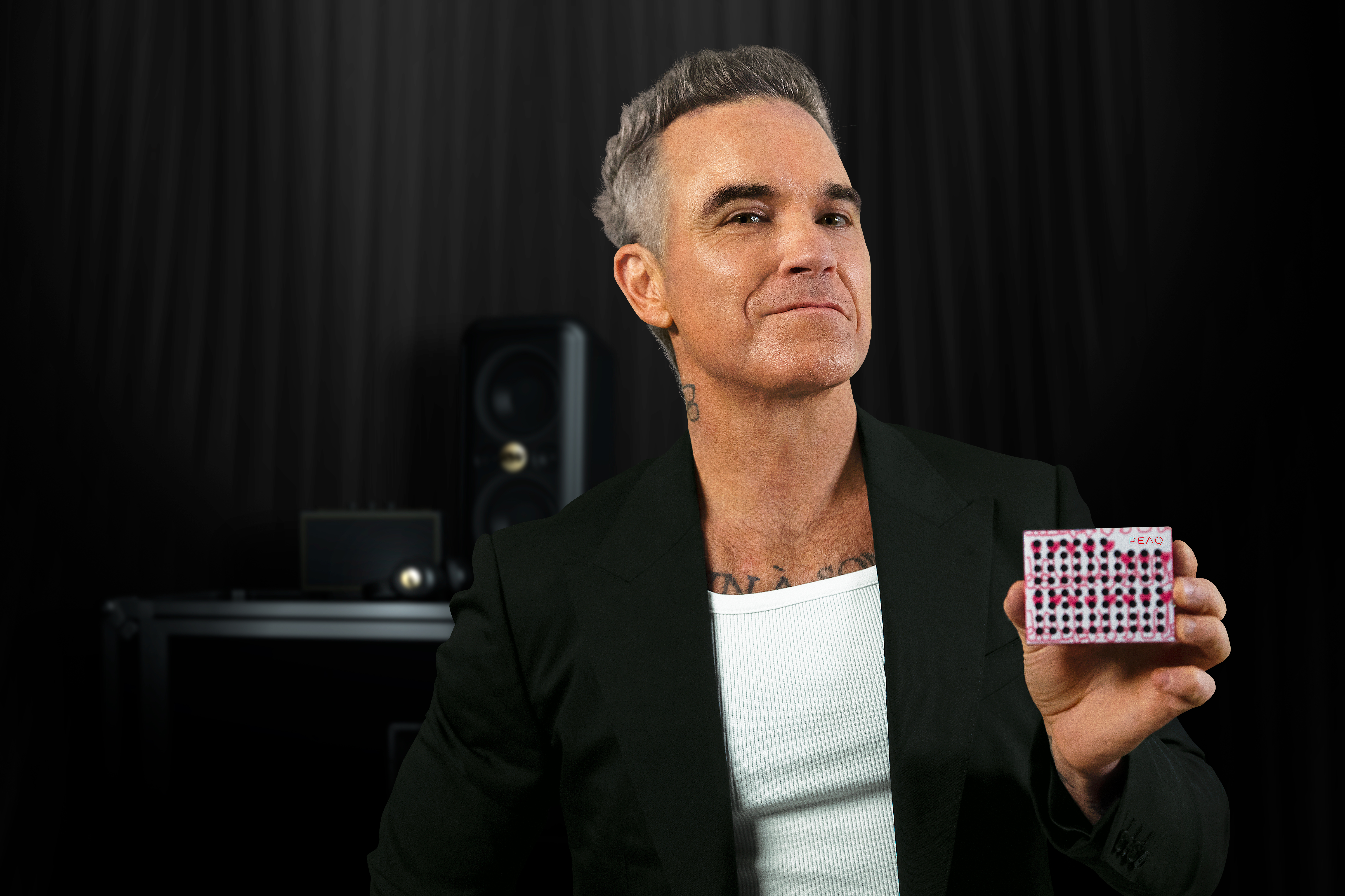 Mann im schwarzen Anzug hält eine Spielkarte mit rosa Punkten und schwarzen Quadraten.