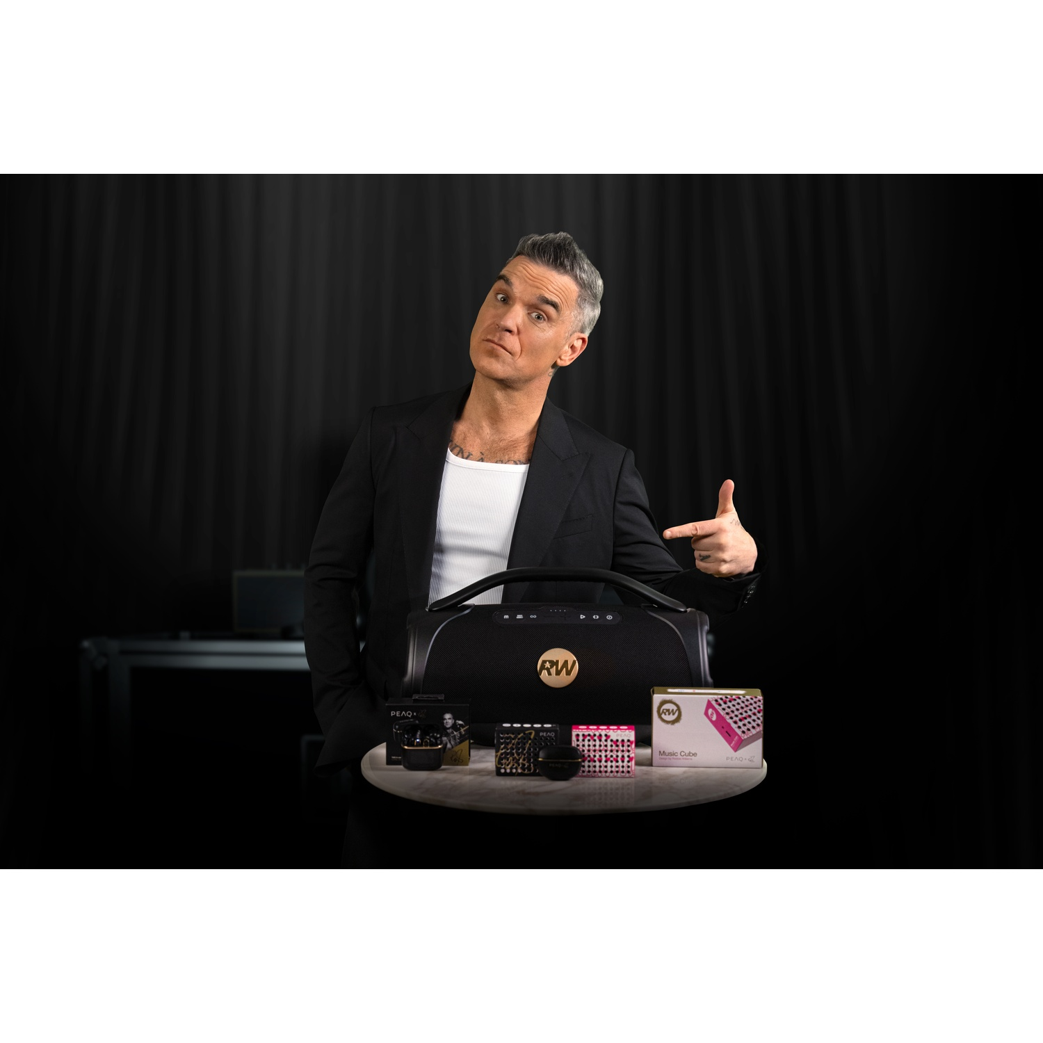 Uomo in abito nero indica un altoparlante portatile e piccole scatole musicali.