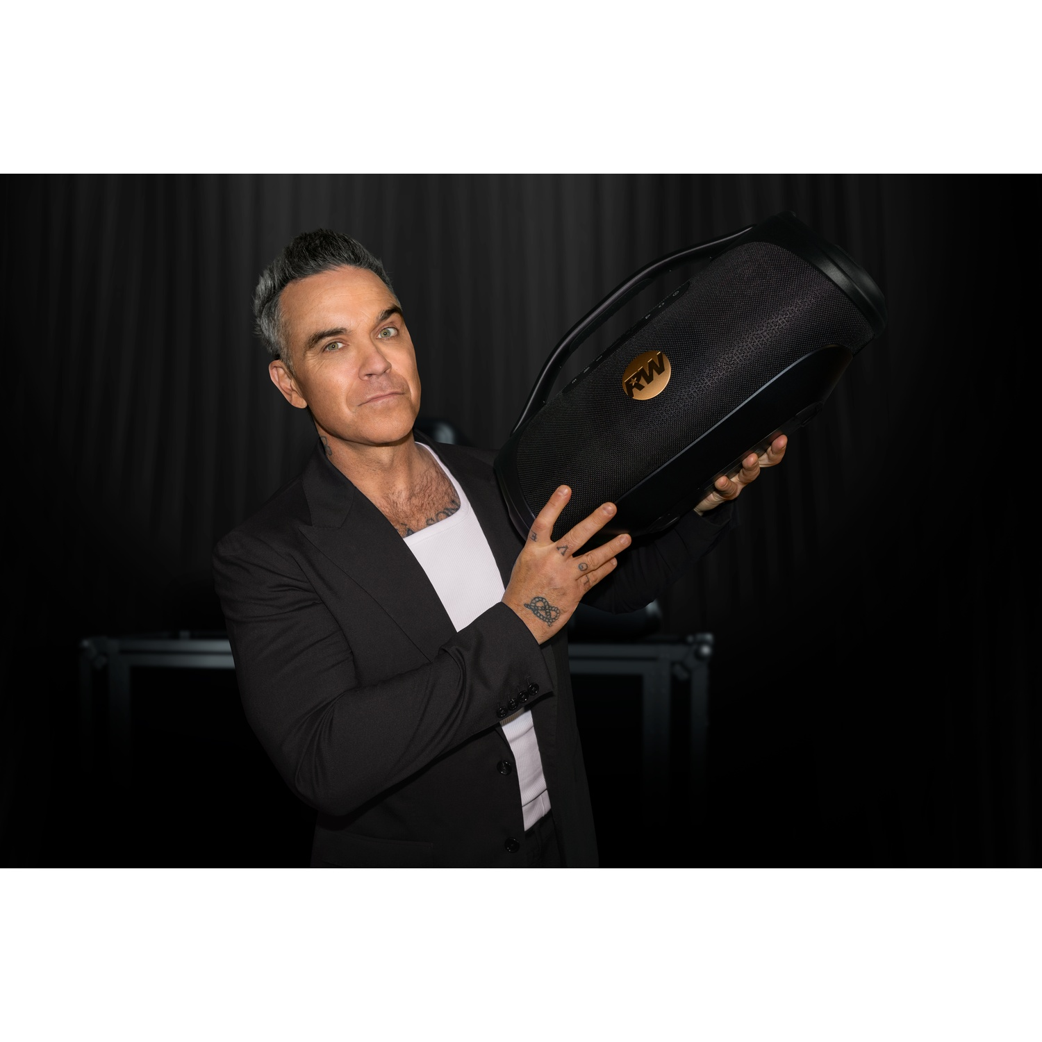 Uomo con capelli grigi tiene uno speaker nero con logo RW.