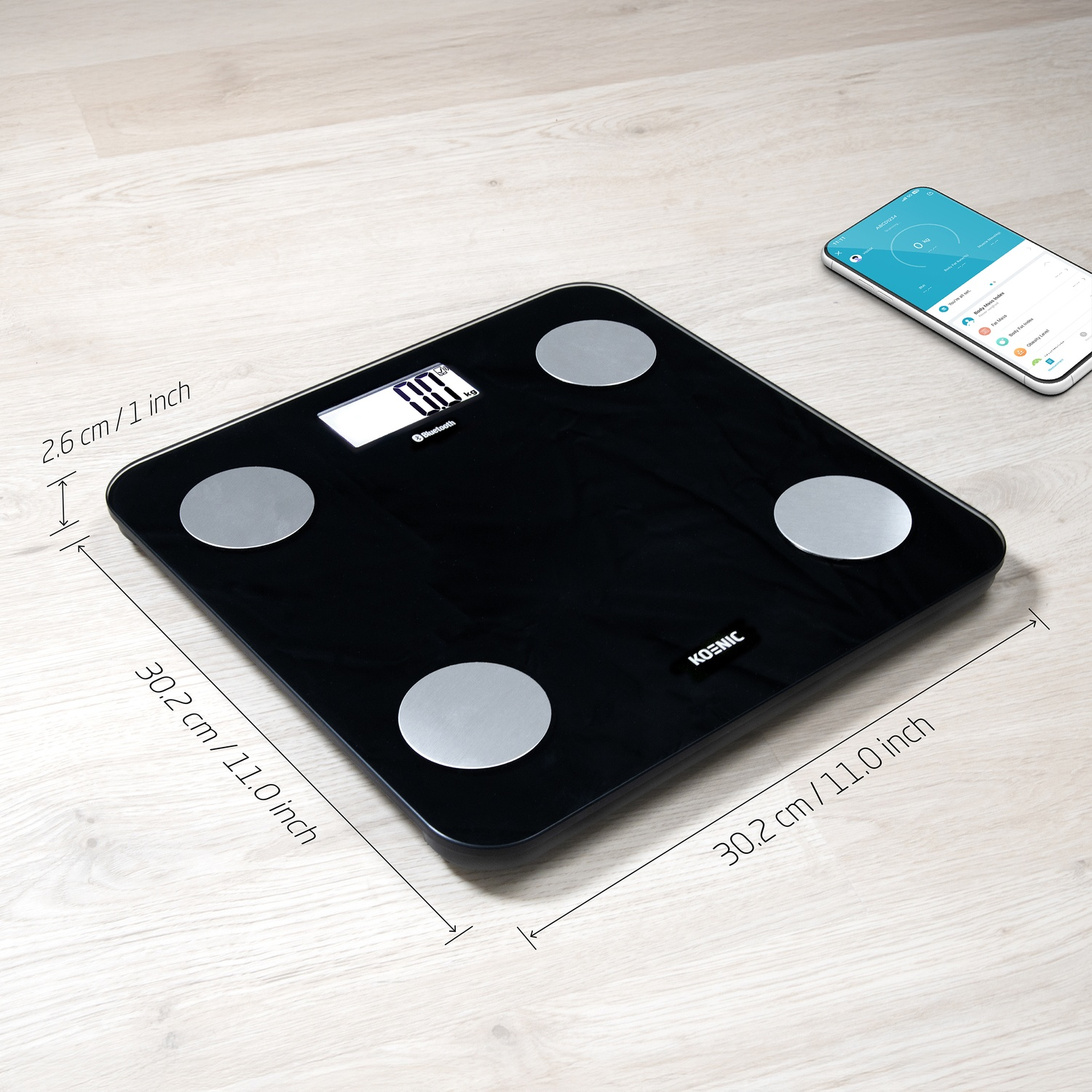 Black personal scale with round metal sensors and display. Smartphone next to it.