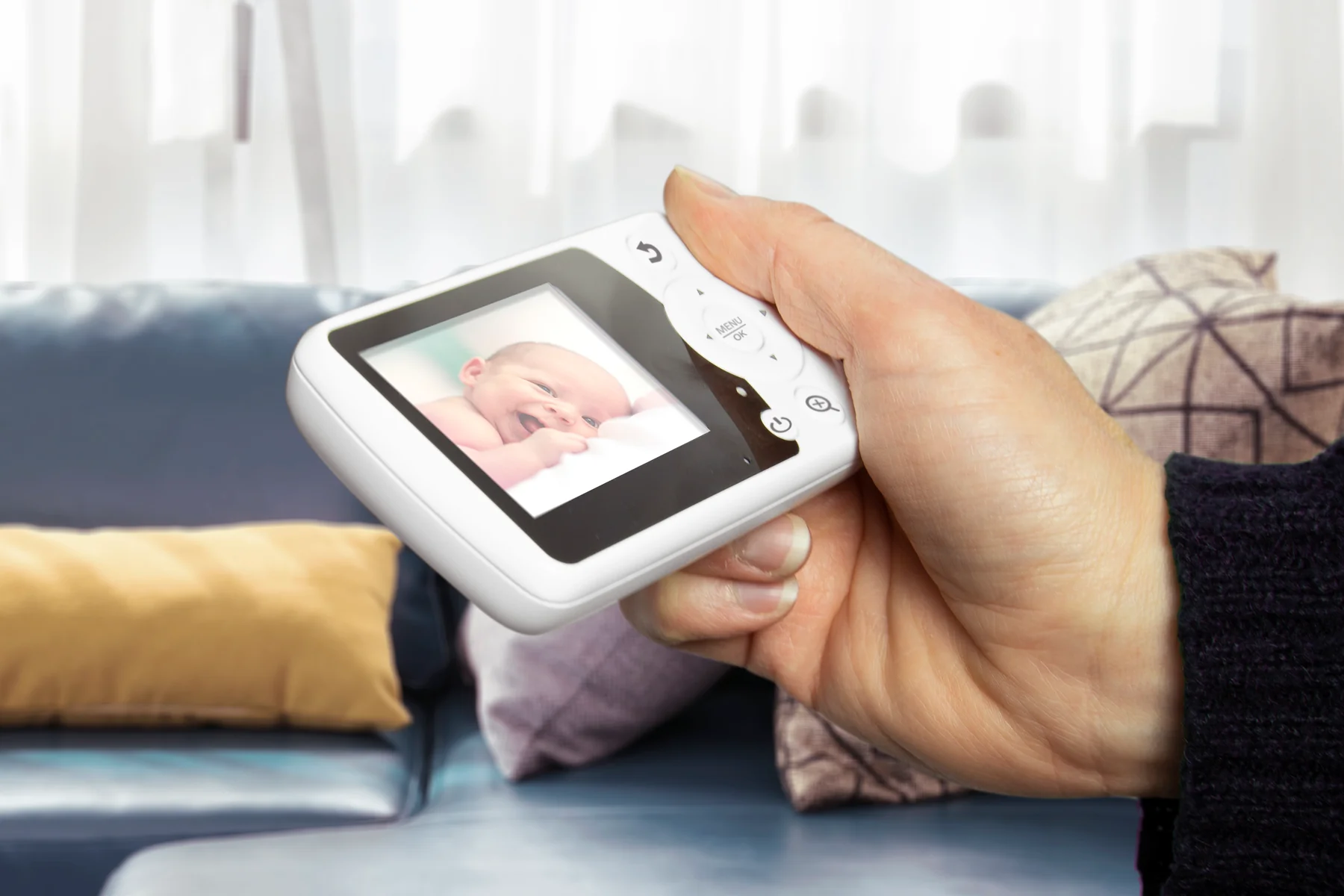 Un bébé sourit sur l'écran d'un babyphone tenu par une main.
