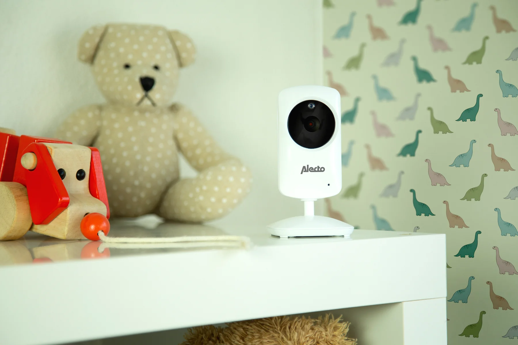 Une baby phone à côté d'un ours en peluche et d'un jouet en bois sur une étagère.