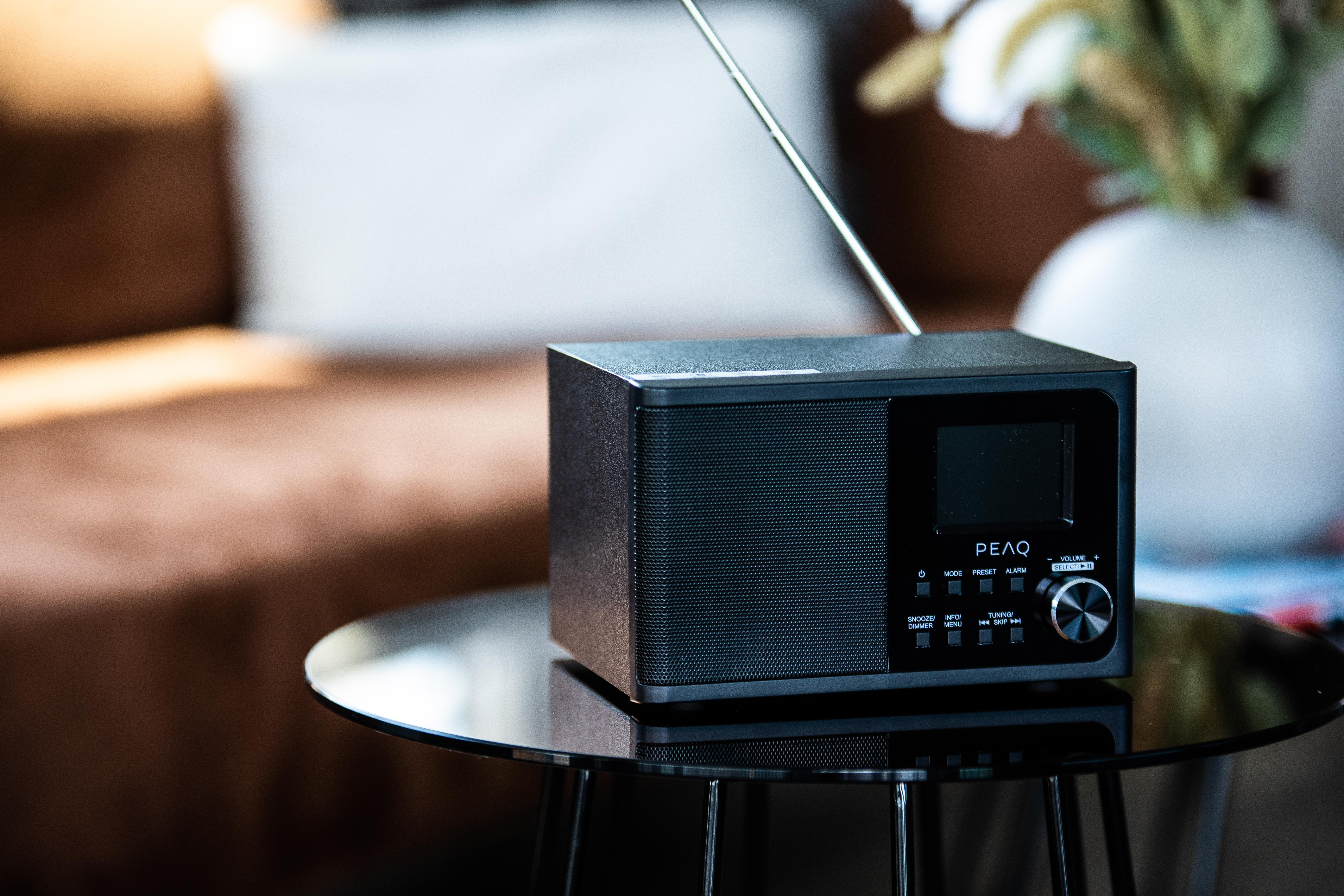 Ein schwarzer Digitalradio mit silberner Antenne steht auf einem Glastisch.