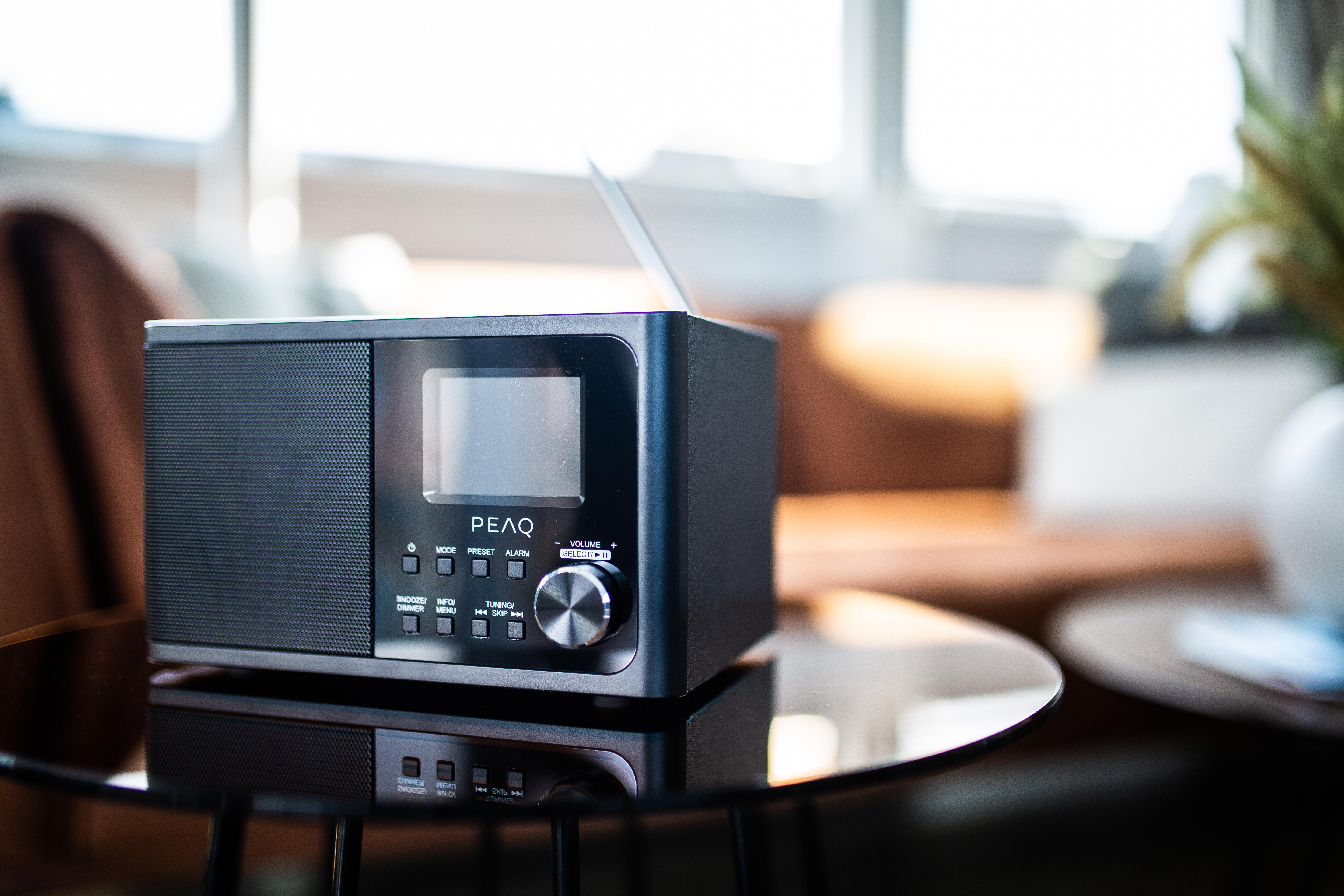 Ein schwarzer PEAQ-Radio auf einem glänzenden Tisch, mit Couch im Hintergrund.