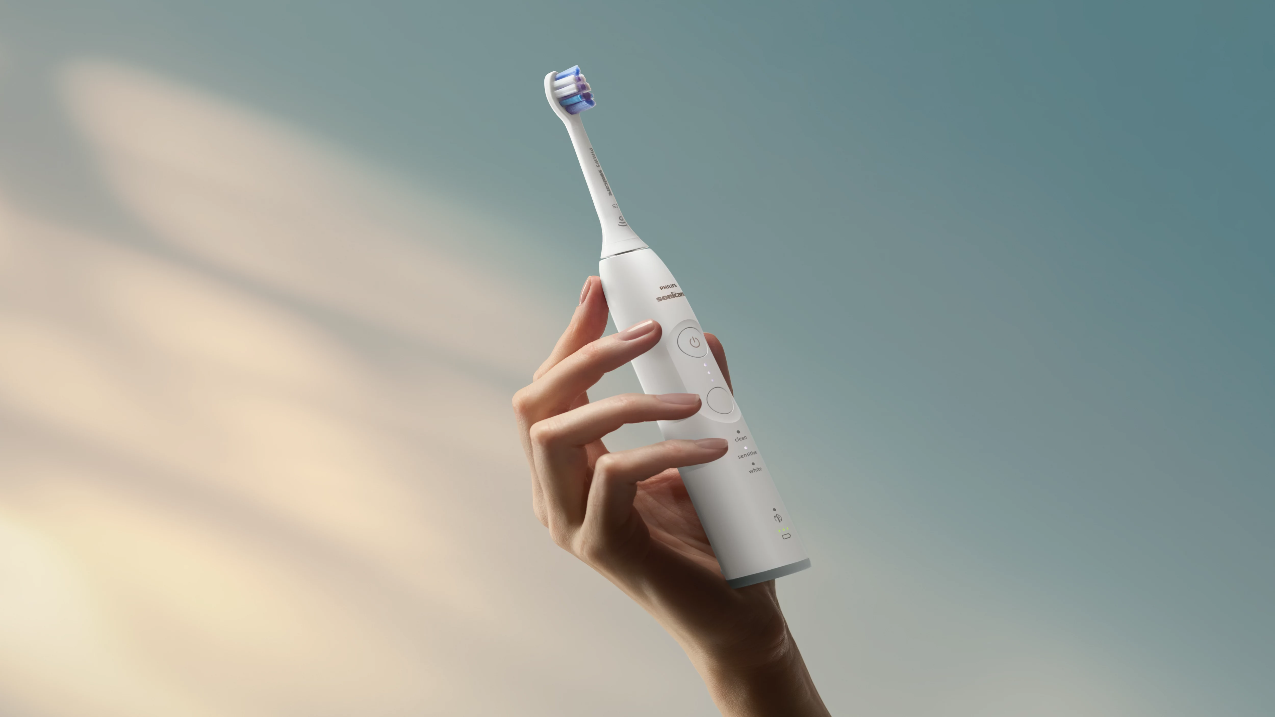 Eine Hand hält eine weiße elektrische Zahnbürste mit blauen Borsten.