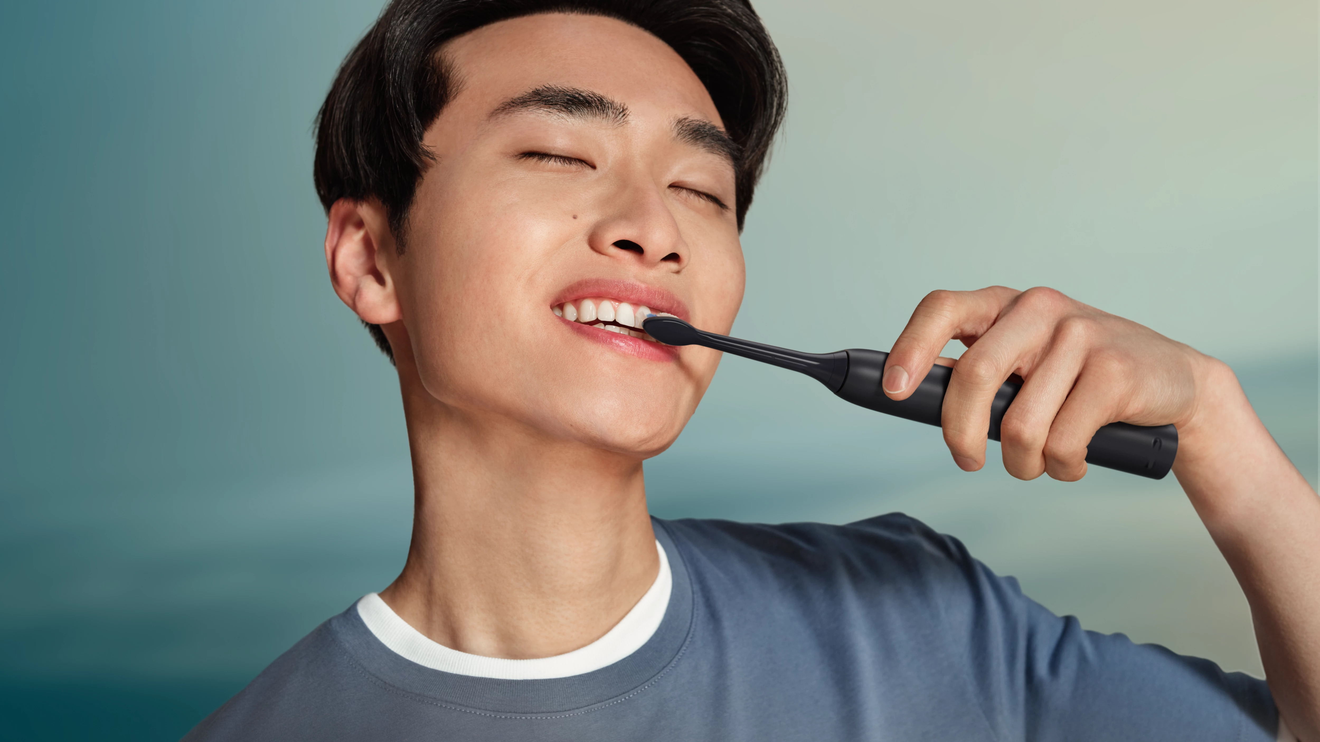 Mężczyzna myje zęby czarną szczoteczką elektryczną.