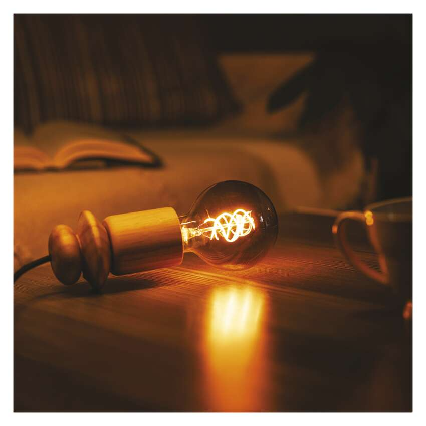 Egy fa talapzaton álló Edison izzós lámpa fekszik egy faasztalon.