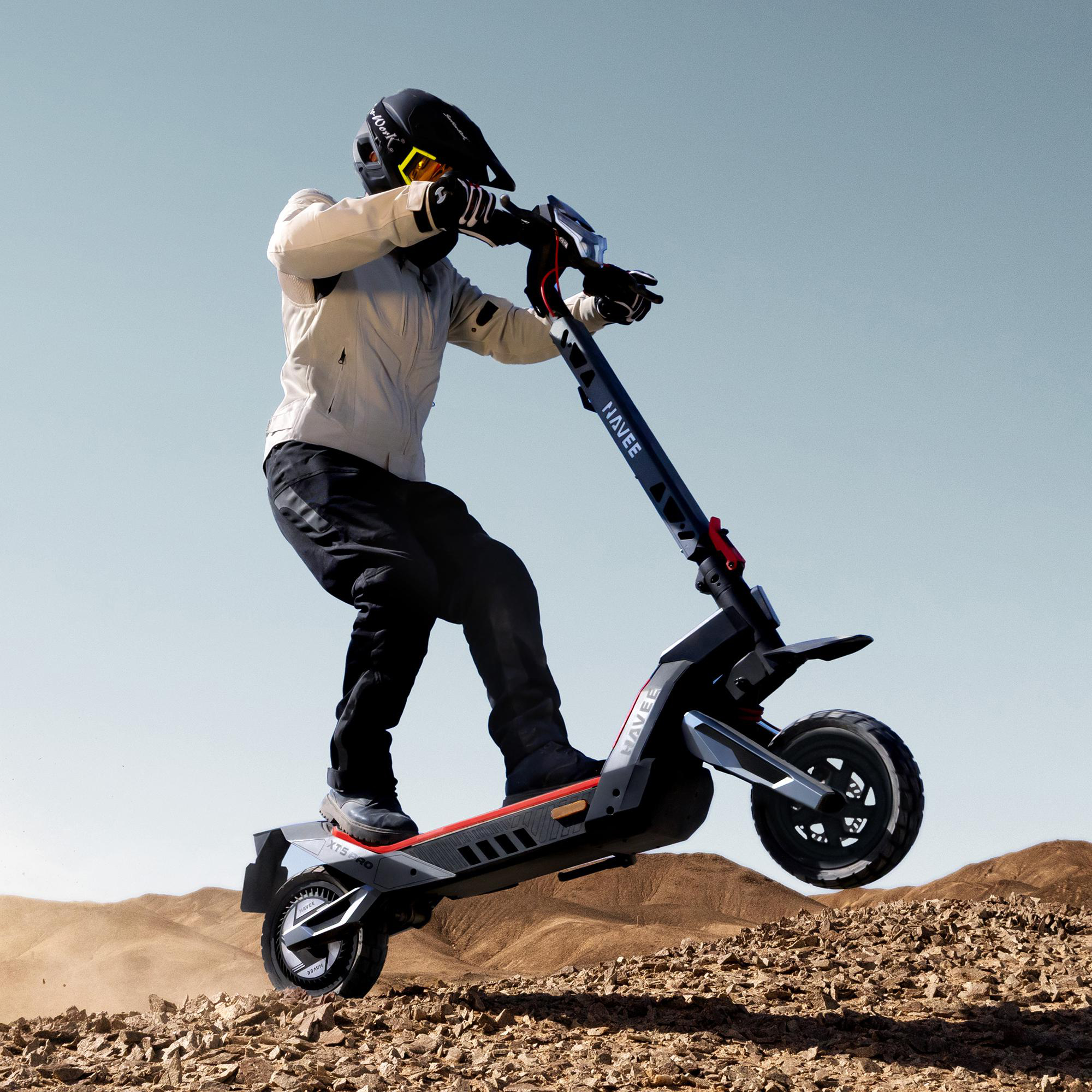 Fahrer in Schutzkleidung springt mit Elektro-Scooter über felsigen Boden.