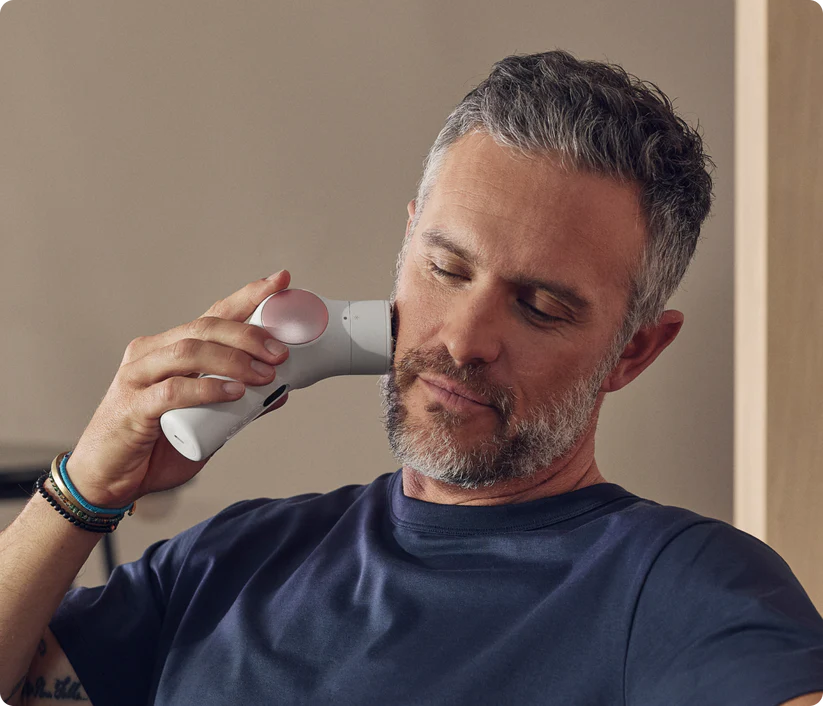 Un hombre con cabello gris usa un dispositivo de masaje facial blanco.