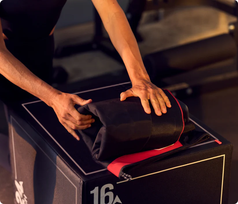 Manos doblando tela negra con borde rojo sobre caja negra en gimnasio.