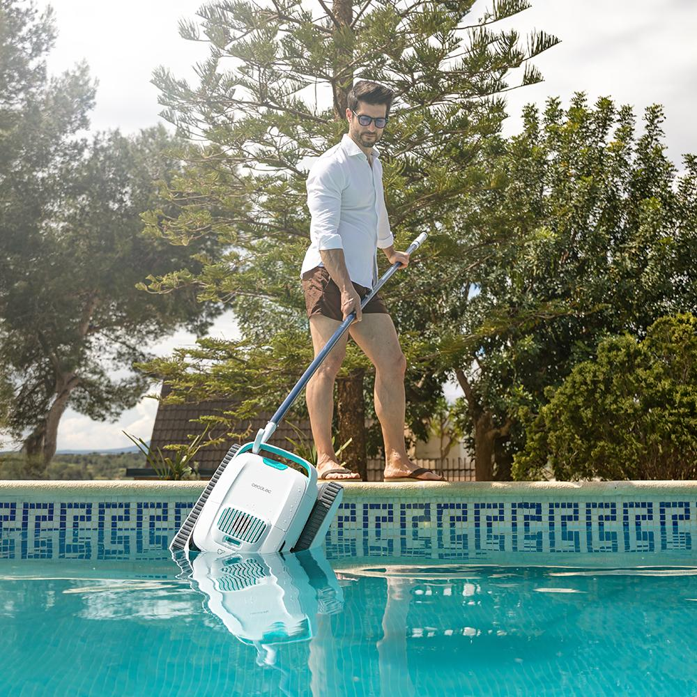 Hombre limpia piscina con robot limpiador en el borde.