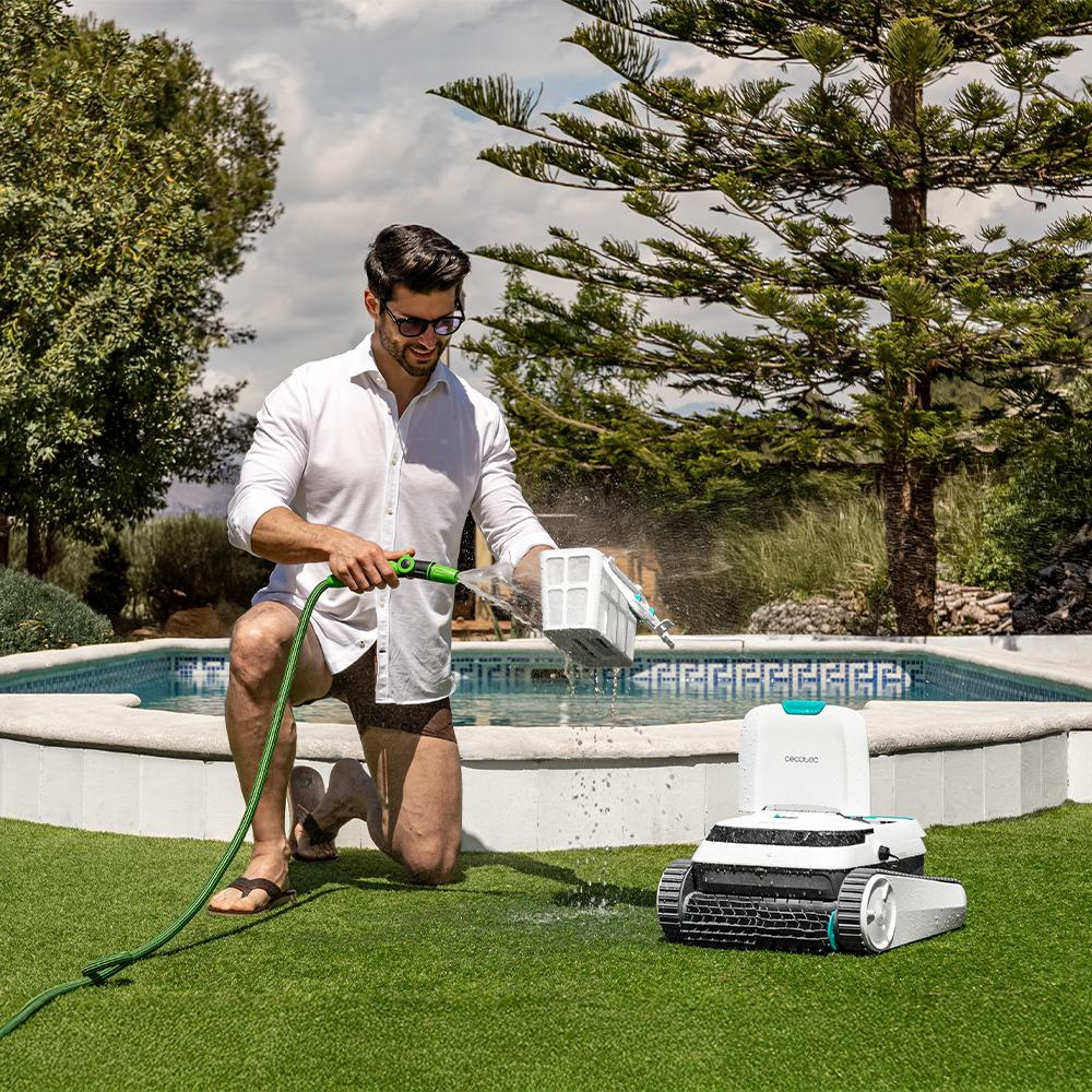 Hombre limpia filtro de robot de piscina con manguera en el jardín.