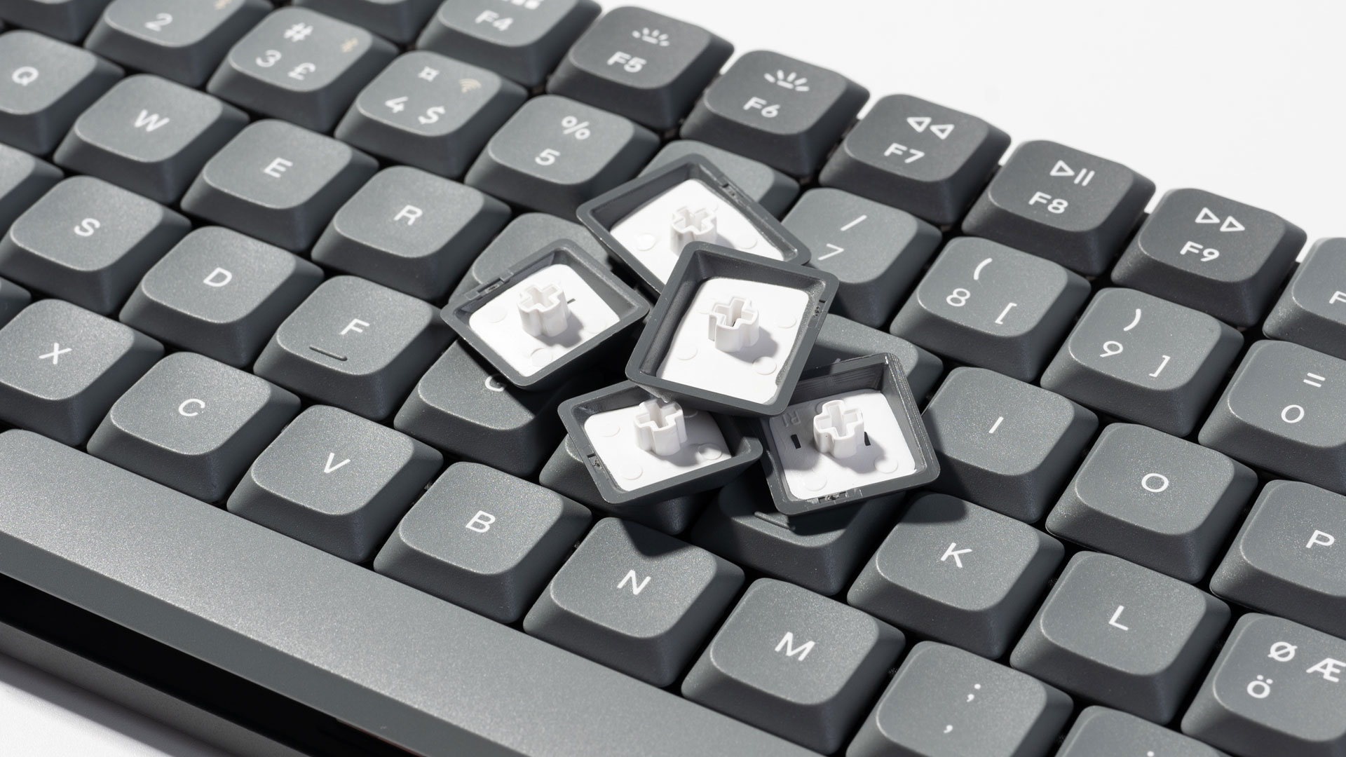 Graue Tastenkappen mit weißen Kreuzstiften liegen auf einer Tastatur.