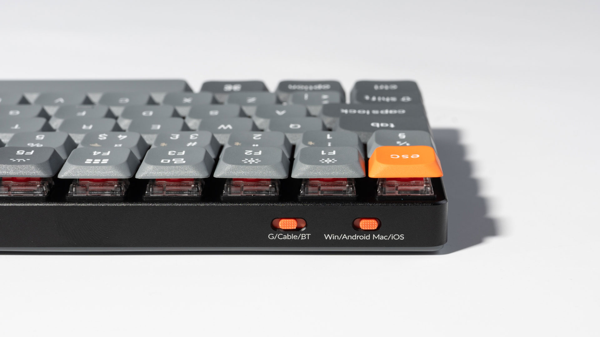 Graue mechanische Tastatur mit orangefarbener ESC-Taste und roten Schaltern.