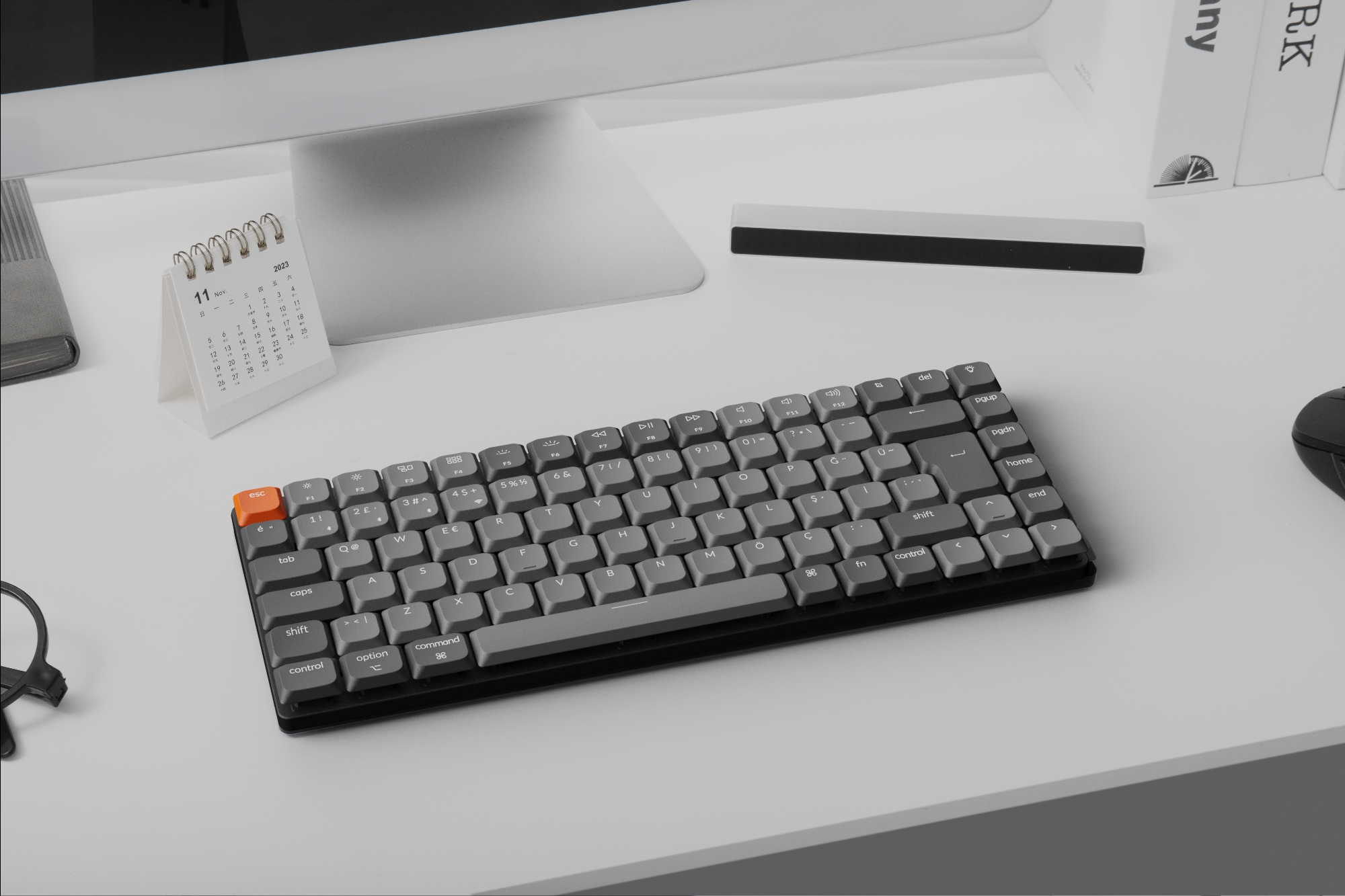 Eine graue mechanische Tastatur mit Kalender und Maus auf einem weißen Schreibtisch.