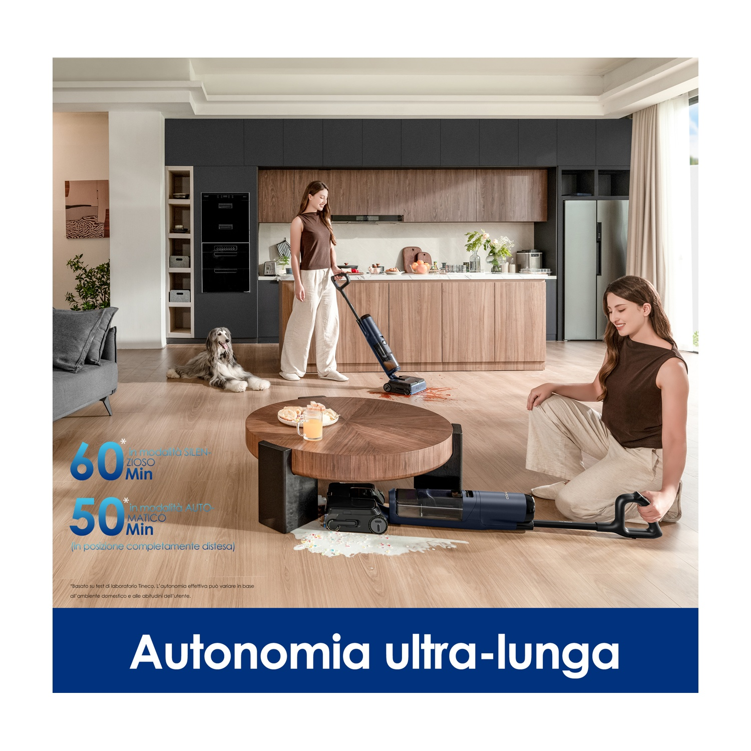 Due donne puliscono tavolo e pavimento cucina con aspirapolvere. Un cane è vicino.