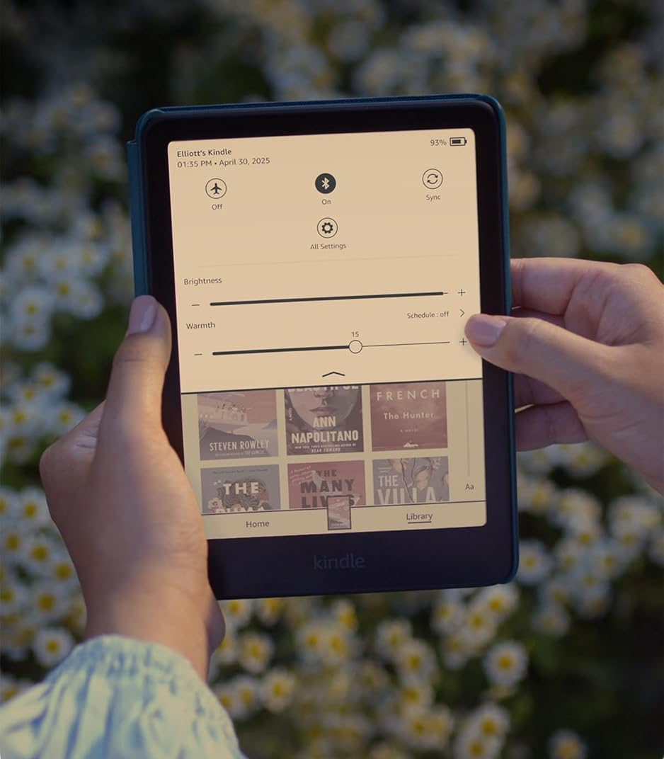 Kezen tartott Kindle e-olvasó beállításokat mutat. Könyvek láthatók alul.