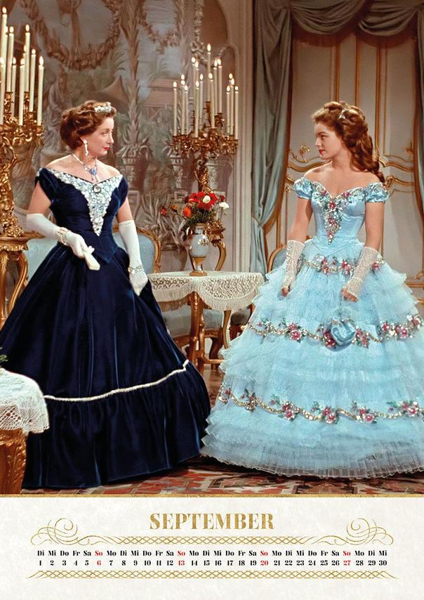 Zwei Frauen in opulenten Kleidern stehen in einem prunkvollen Raum.