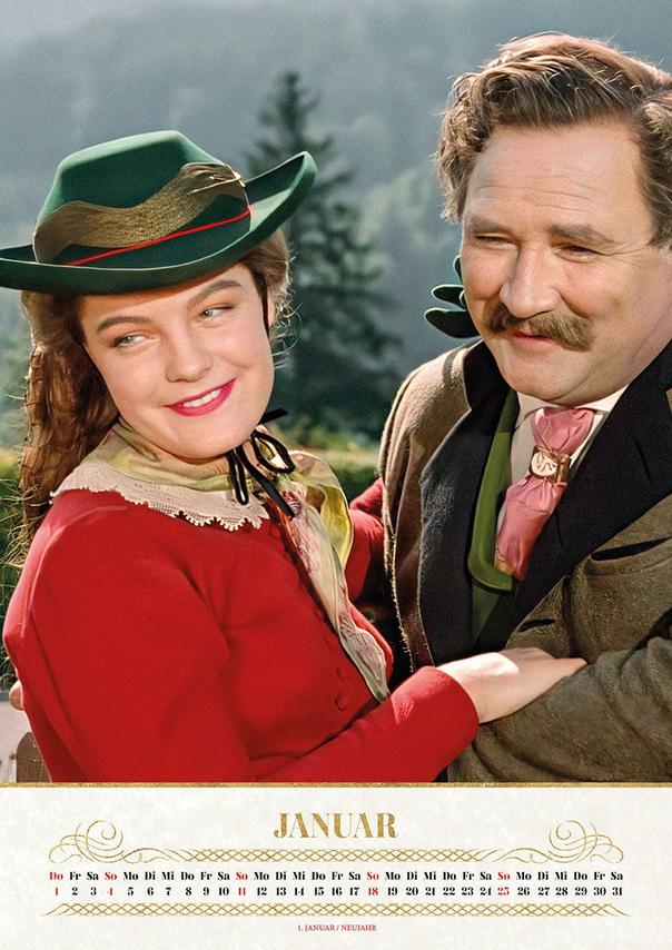 Eine lächelnde Frau mit grünem Hut und rotem Oberteil steht neben einem Mann mit Schnurrbart, beide in traditioneller Kleidung.