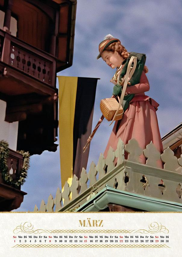 Frau in Tracht auf einem Balkon, mit Fahnen im Hintergrund.