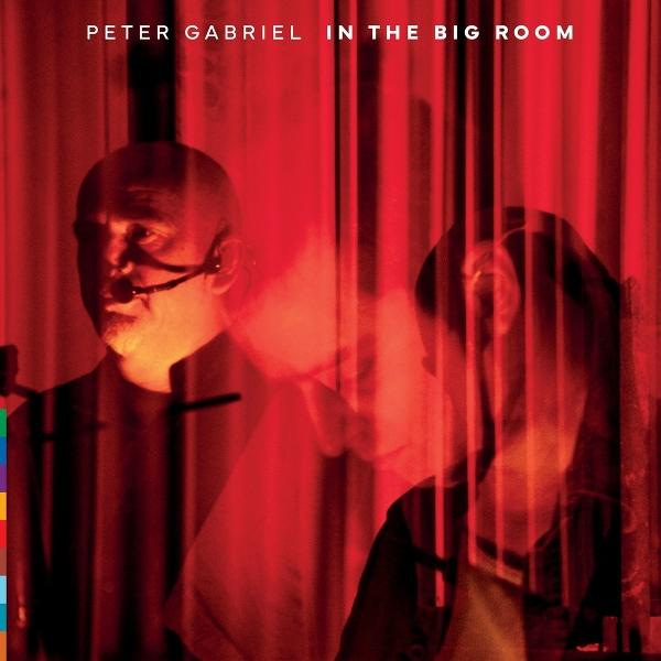 Peter Gabriel mit Mikrofon vor roten Vorhängen, rechts eine weitere Person.