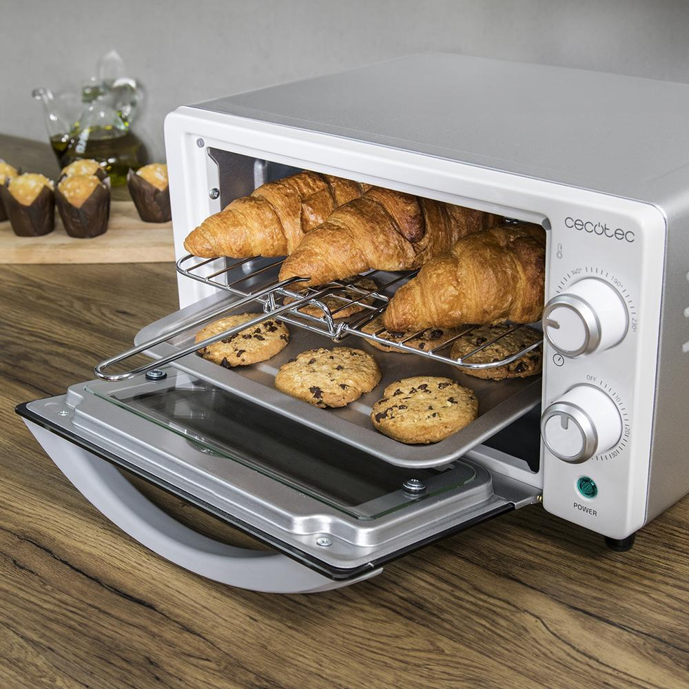 Un horno pequeño con cruasanes y galletas en una rejilla y bandeja.