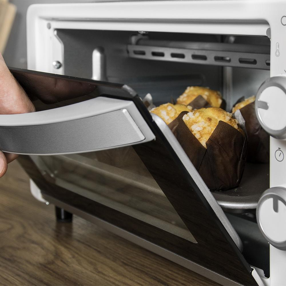 Una mano abre la puerta de un horno que revela muffins en moldes de papel marrones.
