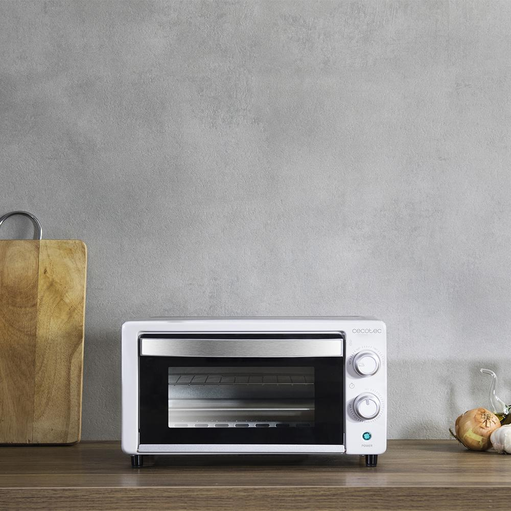 Un horno de sobremesa blanco está sobre un mostrador de madera junto a una tabla de cortar y cebollas.
