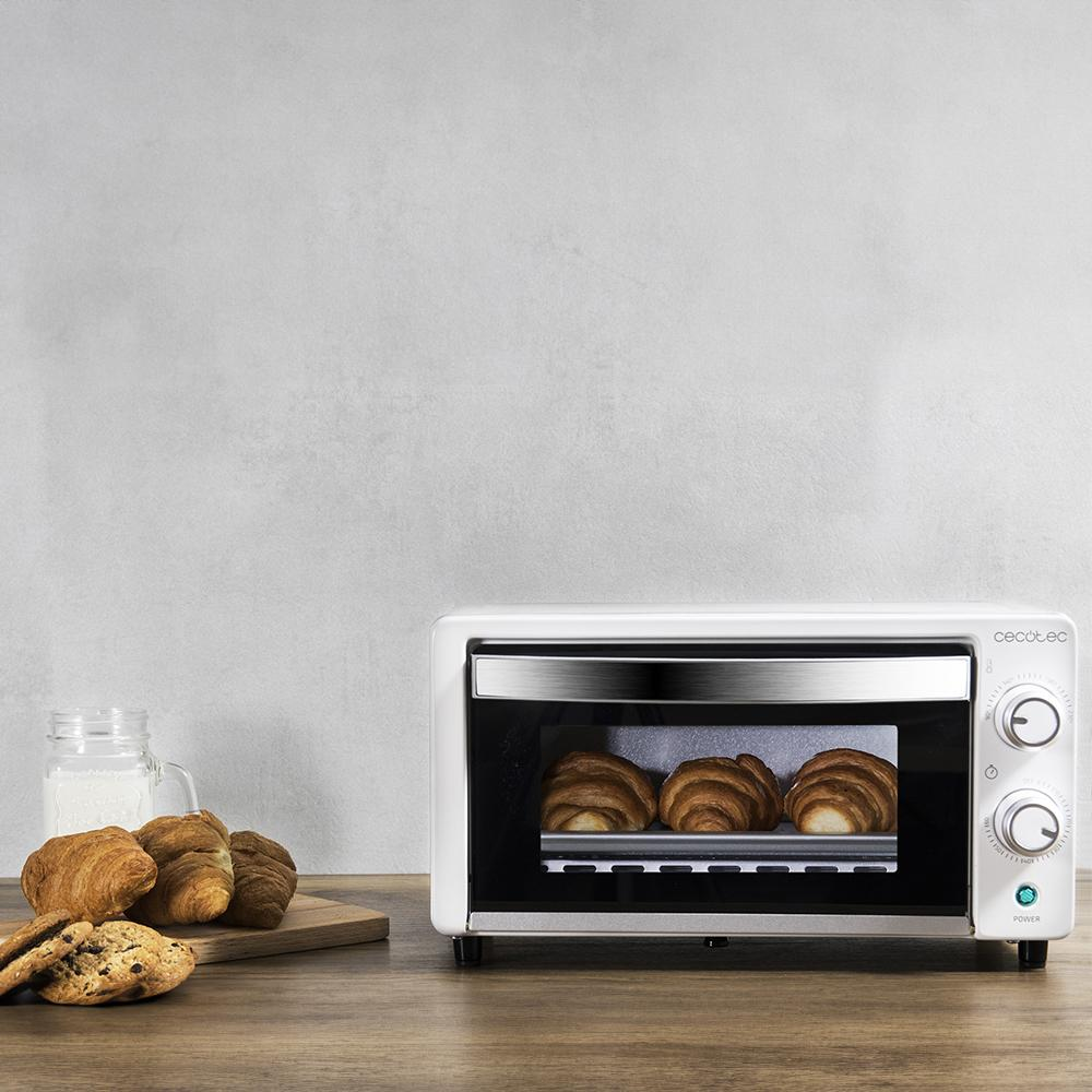 Un horno blanco pequeño con tres cruasanes dentro. Al lado hay galletas y cruasanes.