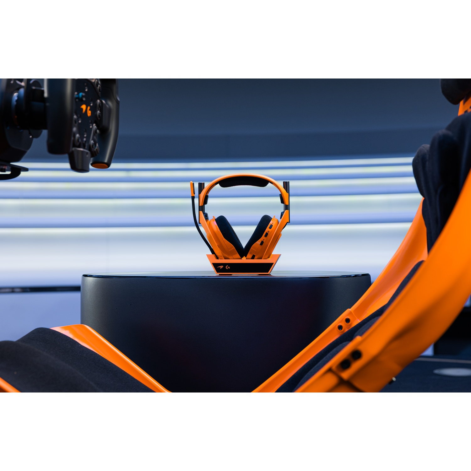 Un headset arancione su piedistallo nero, con volante da corsa e sedile sullo sfondo.