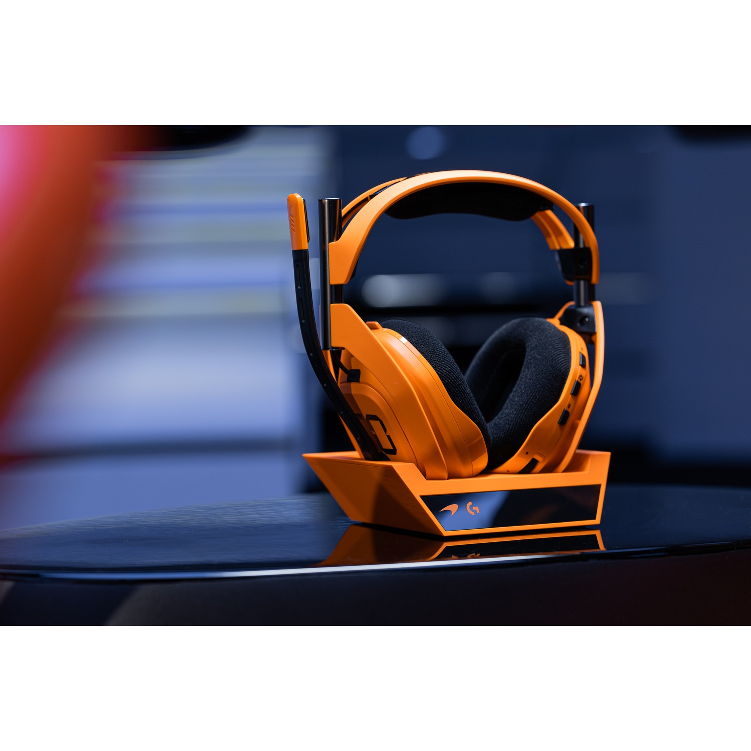 Cuffie arancioni con microfono su supporto nero con illuminazione di sfondo blu.