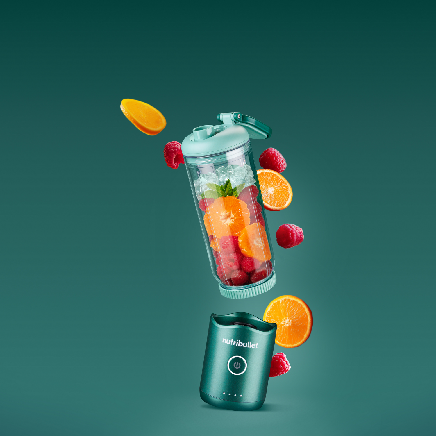 Un vaso de licuadora con fruta y hielo flota sobre la base. Naranjas y frambuesas vuelan.