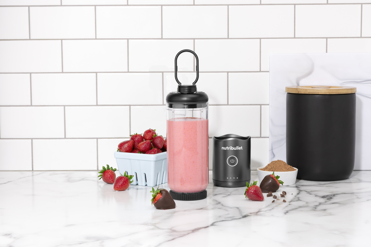 Una licuadora Nutribullet con fresas, fresas bañadas en chocolate y cacao en polvo.